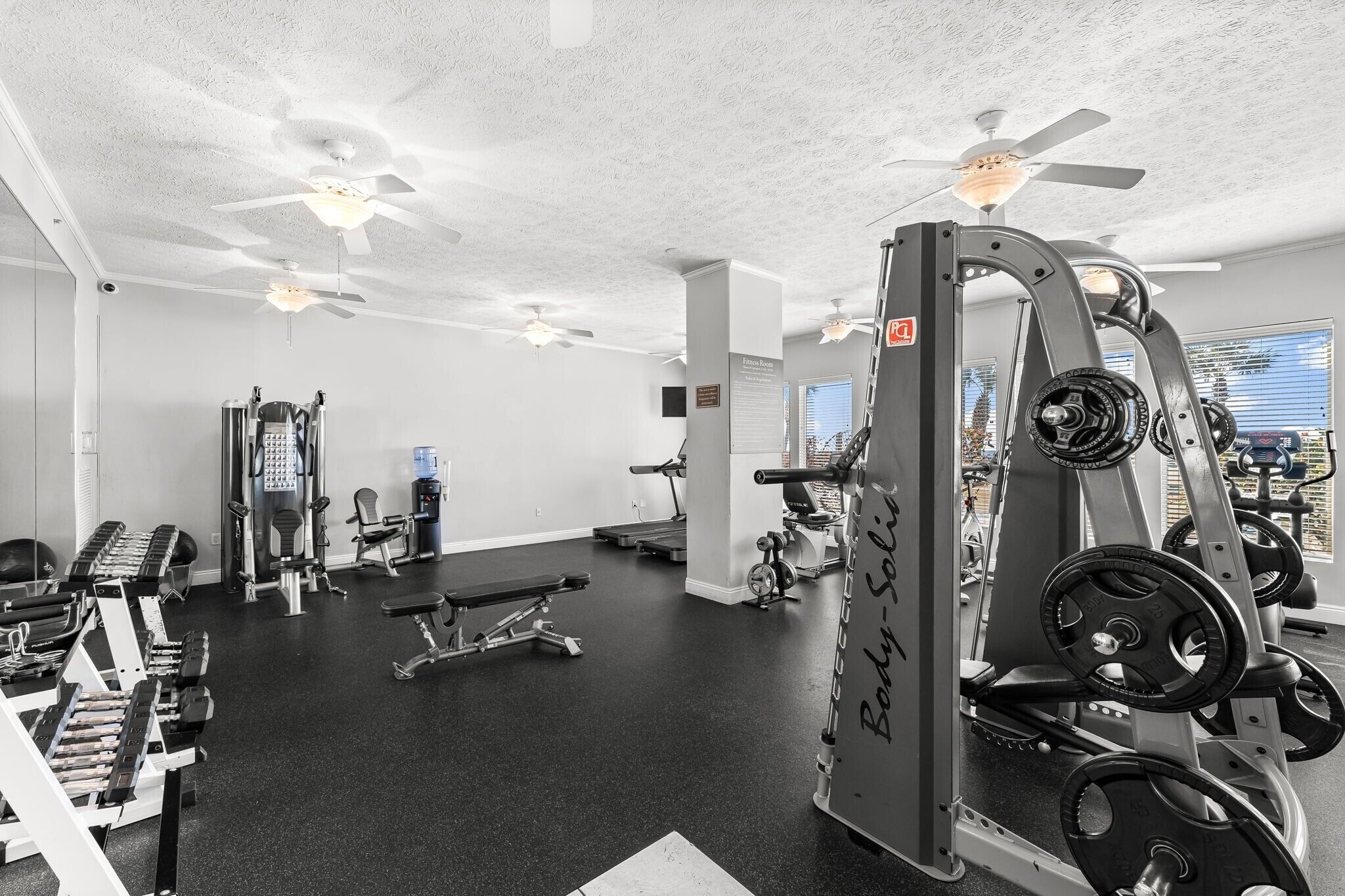A gym with ceiling fans, various exercise equipment, and a view of the outside.