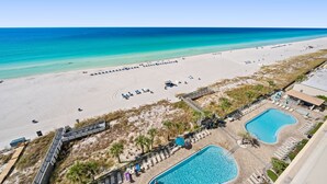A beach resort with a swimming pool, lounge chairs, and a view of the ocean.