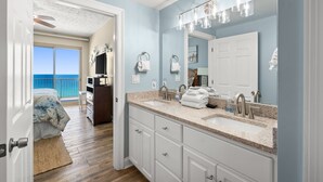 A bathroom with a large mirror, two sinks, and a view of the ocean through an open door.