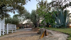 A rustic outdoor area with a stone pathway, wooden fence, and various trees. - Zeytinlibahçe Konukevi (Bozcaada)