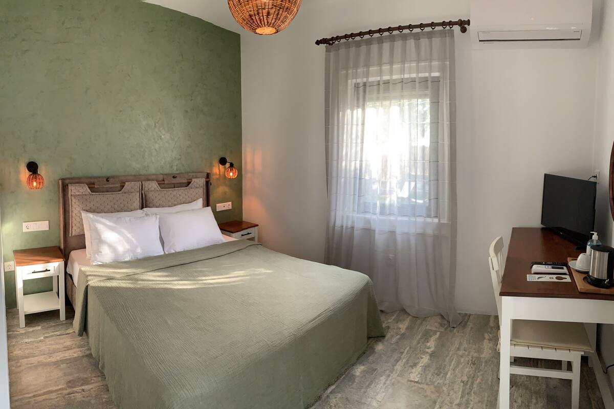 Une chambre à coucher bien rangée, avec un lit, des tables de chevet, un bureau, une télévision et une fenêtre avec des rideaux.