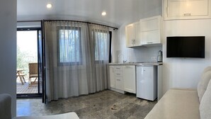 A compact kitchen with white cabinets, a built-in dishwasher, and a flat-screen TV mounted on the wall. - Zeytinlibahçe Konukevi (Bozcaada)
