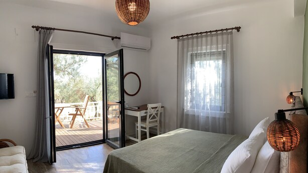 A bedroom with a bed, a desk, and a view through a glass door to an outdoor deck. - Zeytinlibahçe Konukevi (Bozcaada)