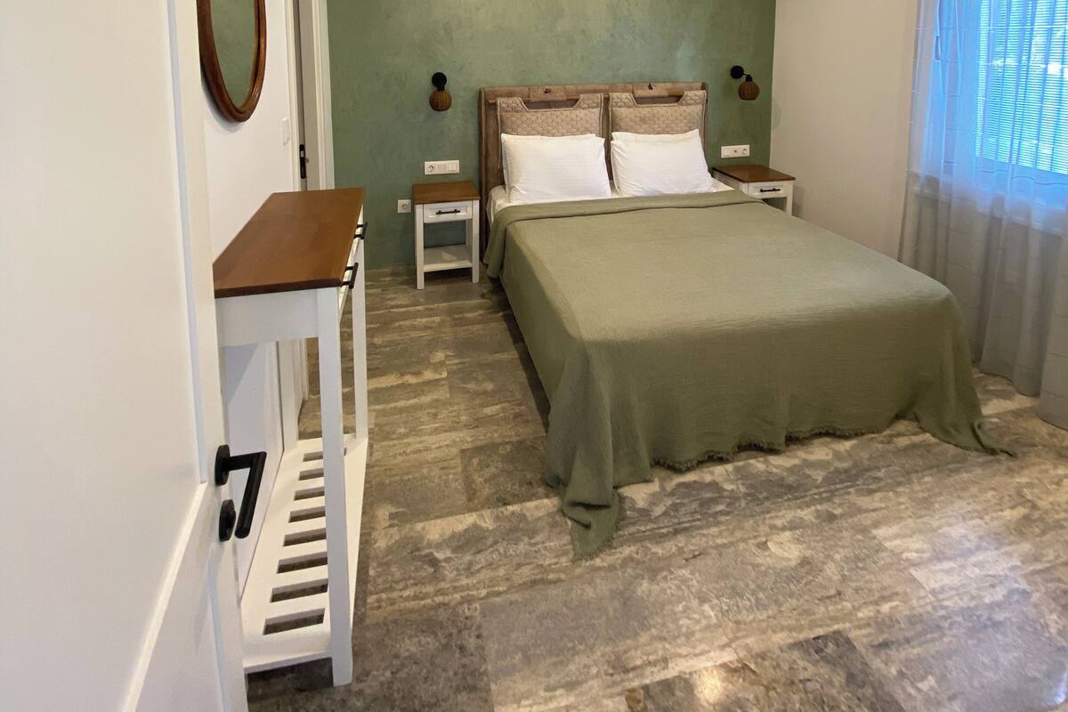 Une chambre à coucher avec un lit, des tables de chevet, un miroir et une fenêtre avec des rideaux.