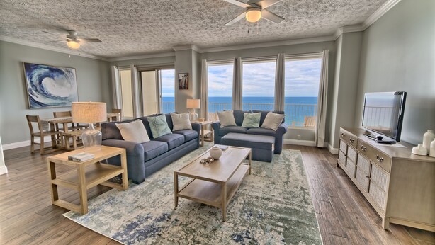 A spacious living room with a large window overlooking the ocean, a ceiling fan, and a television on a cabinet.