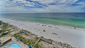 A beach with a swimming pool, lounge chairs, and a lifeguard tower.