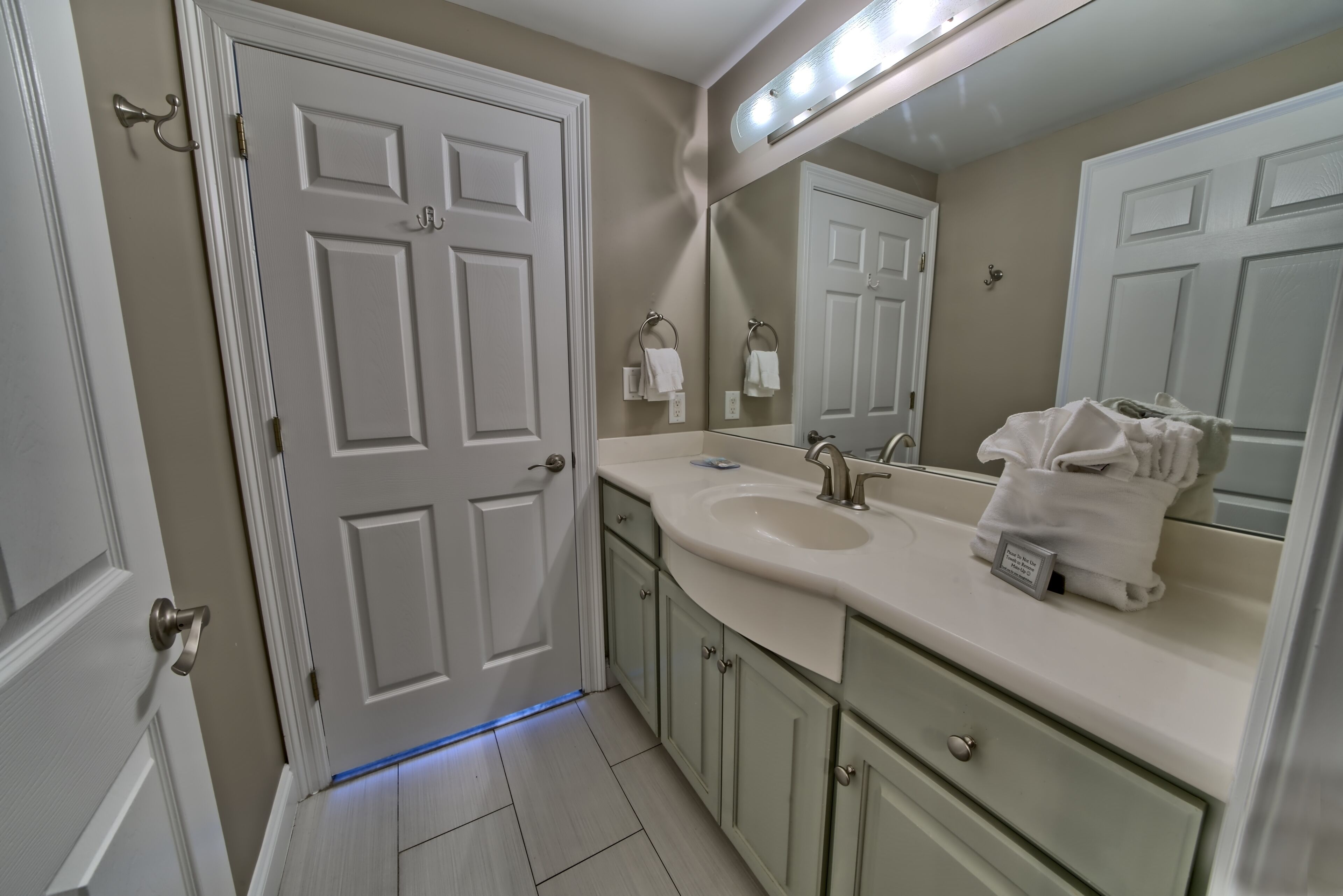 A bathroom with a white door, a sink with a mirror, and a towel rack.