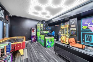 Un salón de juegos con varias máquinas, un área de descanso y una pared decorada con carteles de videojuegos.