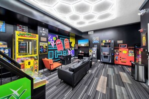 Un salón de juegos con máquinas recreativas, televisor y sofá.
