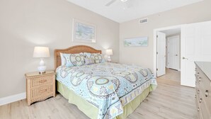 A bedroom with a bed, two bedside tables, a ceiling fan, and a door leading to another room.