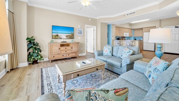 A living room with a sofa, coffee table, and a television. There is a kitchen area with cabinets and a microwave.