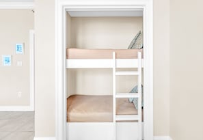 Una cama litera con escalera, paredes color beige y una puerta con interruptor de luz.