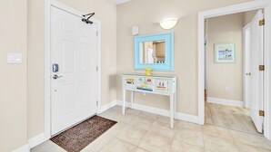 A hallway with a white door, a small table with a mirror, and a light fixture above it.