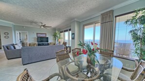 Ein geräumiges Wohnzimmer mit einem Esstisch mit Glasplatte, umgeben von Korbstühlen, einem grauen Sofa und einem Flachbildfernseher.
