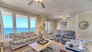 A spacious living room with a large window overlooking the ocean, a ceiling fan, and a view of the sea. - Gulf Crest 502 | Your 2BR Escape on the Gulf!! Beach Service** (Panama City Beach)