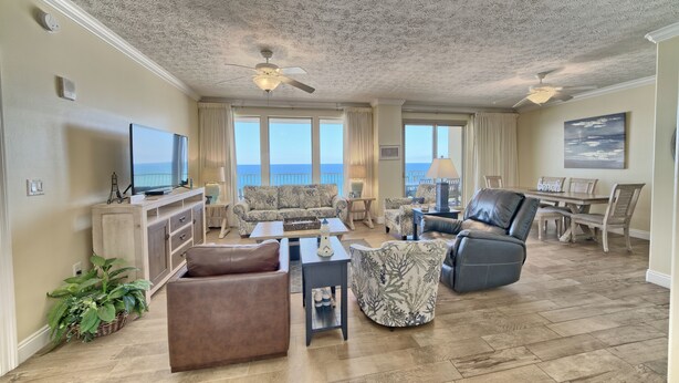 A spacious living room with a large television, comfortable seating, a dining area, and a view of the ocean. - Gulf Crest 502 | Your 2BR Escape on the Gulf!! Beach Service** (Panama City Beach)
