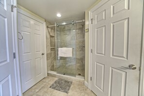 Un baño con cabina de ducha de vidrio, una toalla blanca colgada en la puerta de la ducha y un tapete gris en el suelo.