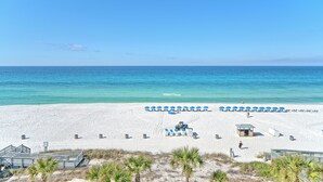 A beach with white sand, clear blue water, and blue umbrellas. There are lounge chairs and a small structure on the beach. - Gulf Crest 502 | Your 2BR Escape on the Gulf!! Beach Service** (Panama City Beach)