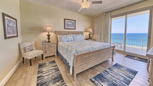 A bedroom with a large bed, two bedside tables, a chair, and a view of the ocean through a balcony. - Gulf Crest 502 | Your 2BR Escape on the Gulf!! Beach Service** (Panama City Beach)