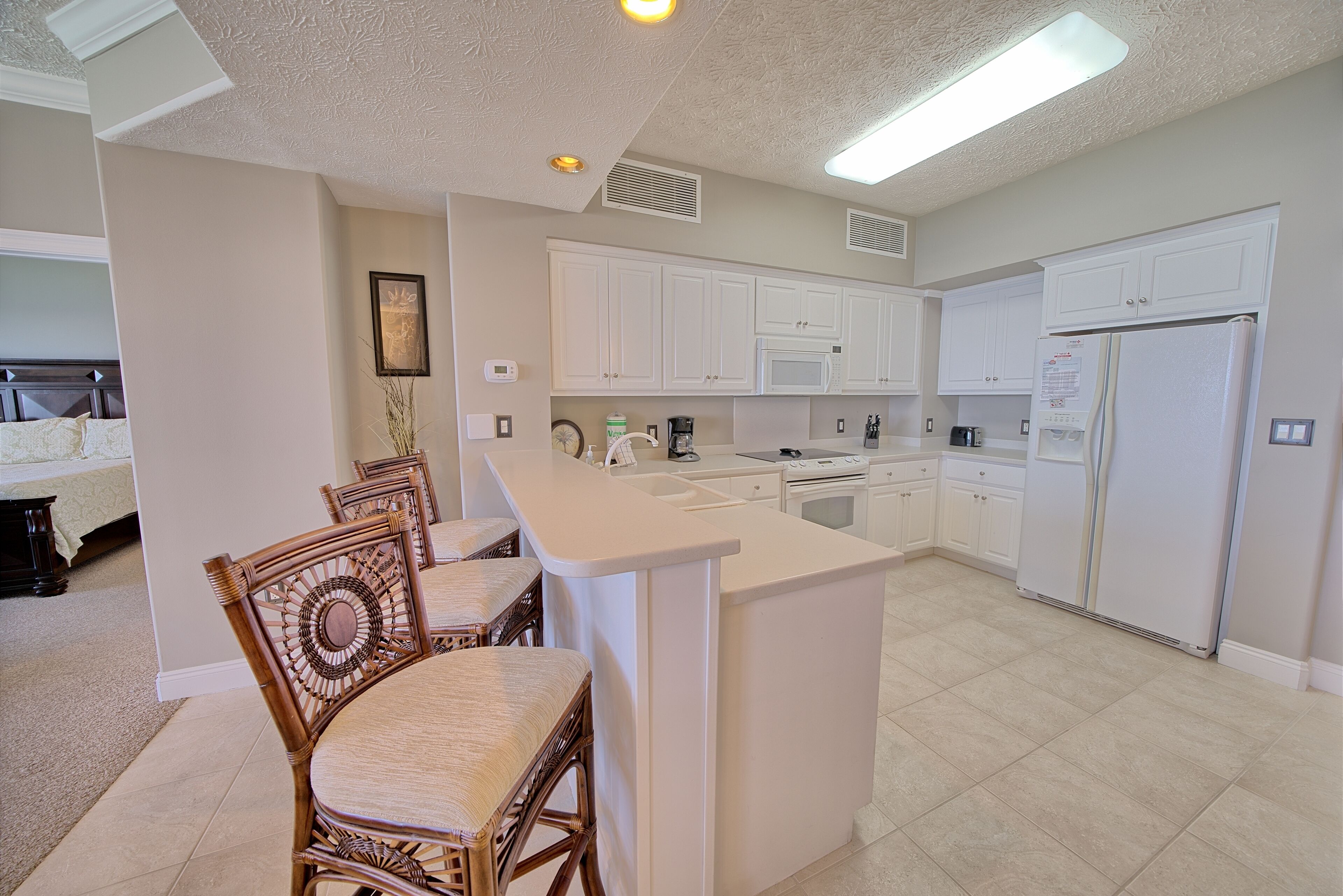 A modern kitchen with white cabinetry, a central island, and a dining area with wicker chairs.