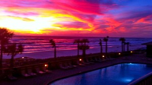 Ein Sonnenuntergang über einem Strand mit Pool und Liegestühlen.