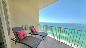 Ein Balkon mit zwei Korbstühlen, jeweils mit einem roten Kissen, Blick auf einen Strand mit klarem, türkisfarbenem Wasser.