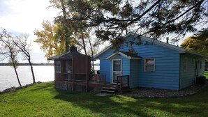 A small blue cabin with a porch, situated by a lake.