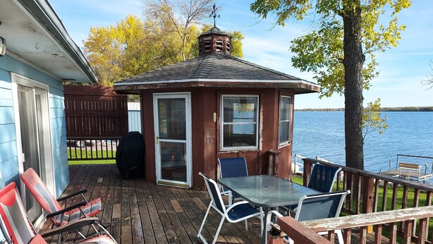 A deck with a table and chairs, a covered grill, and a view of the water.