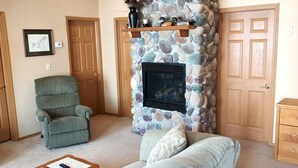A living room with a stone fireplace, a grey armchair, a sofa, and a wooden coffee table.