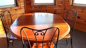 A wooden cabin interior with a round dining table and four metal chairs.