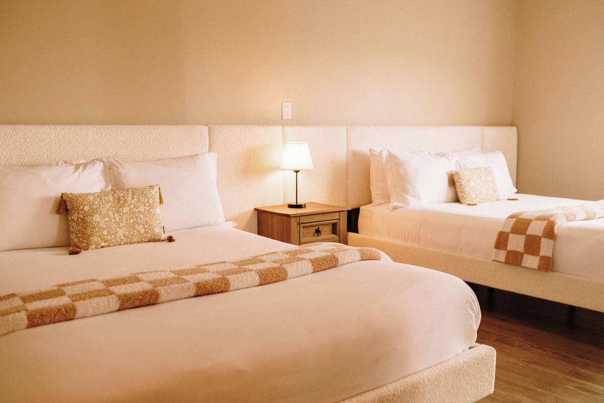 Ein Hotelzimmer mit zwei Betten, einem Nachttisch mit Lampe und einer karierten Decke.