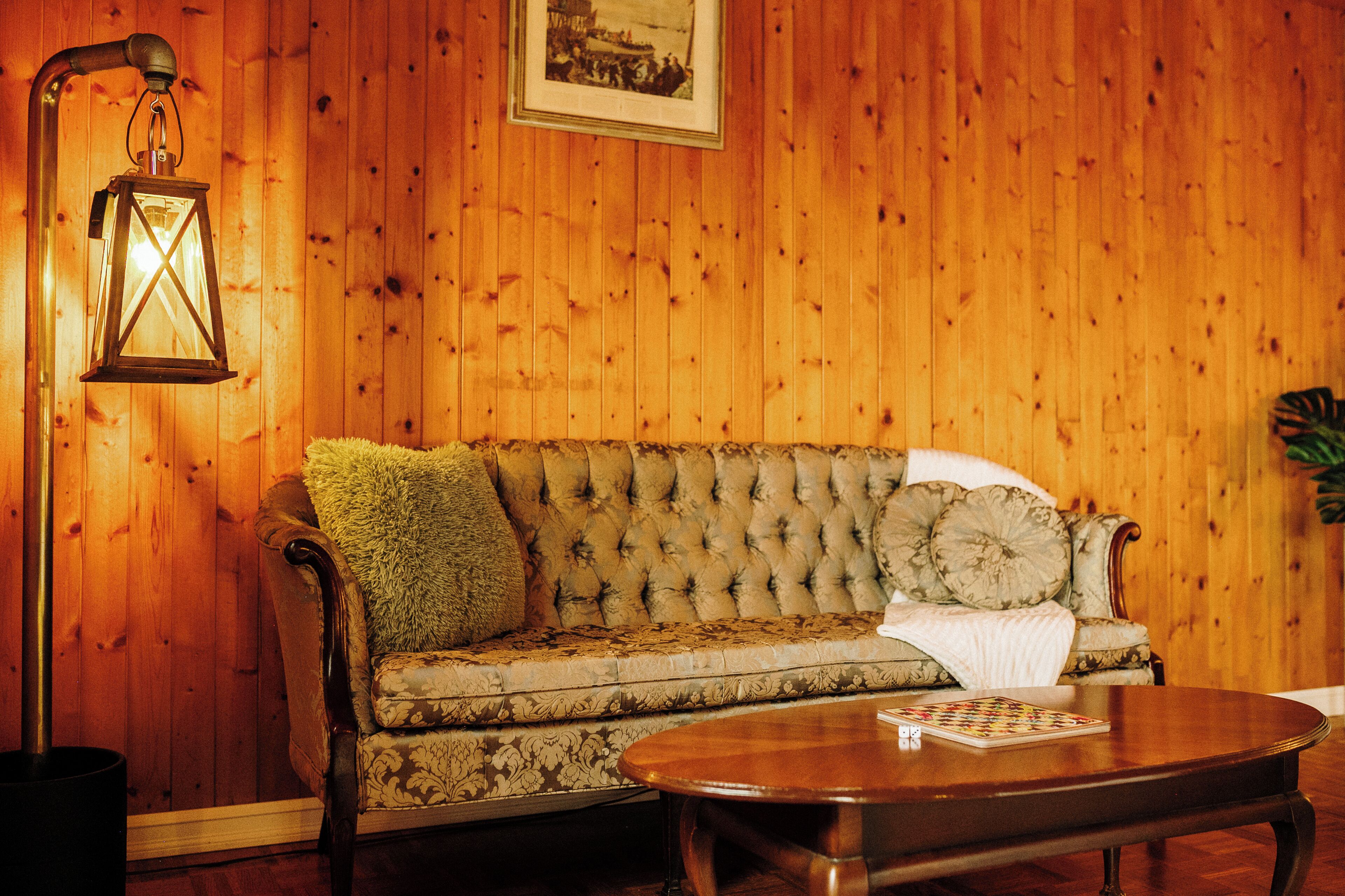 Una habitación con paneles de madera, un sofá capitonado, una mesa de centro de madera y un farol colgante.