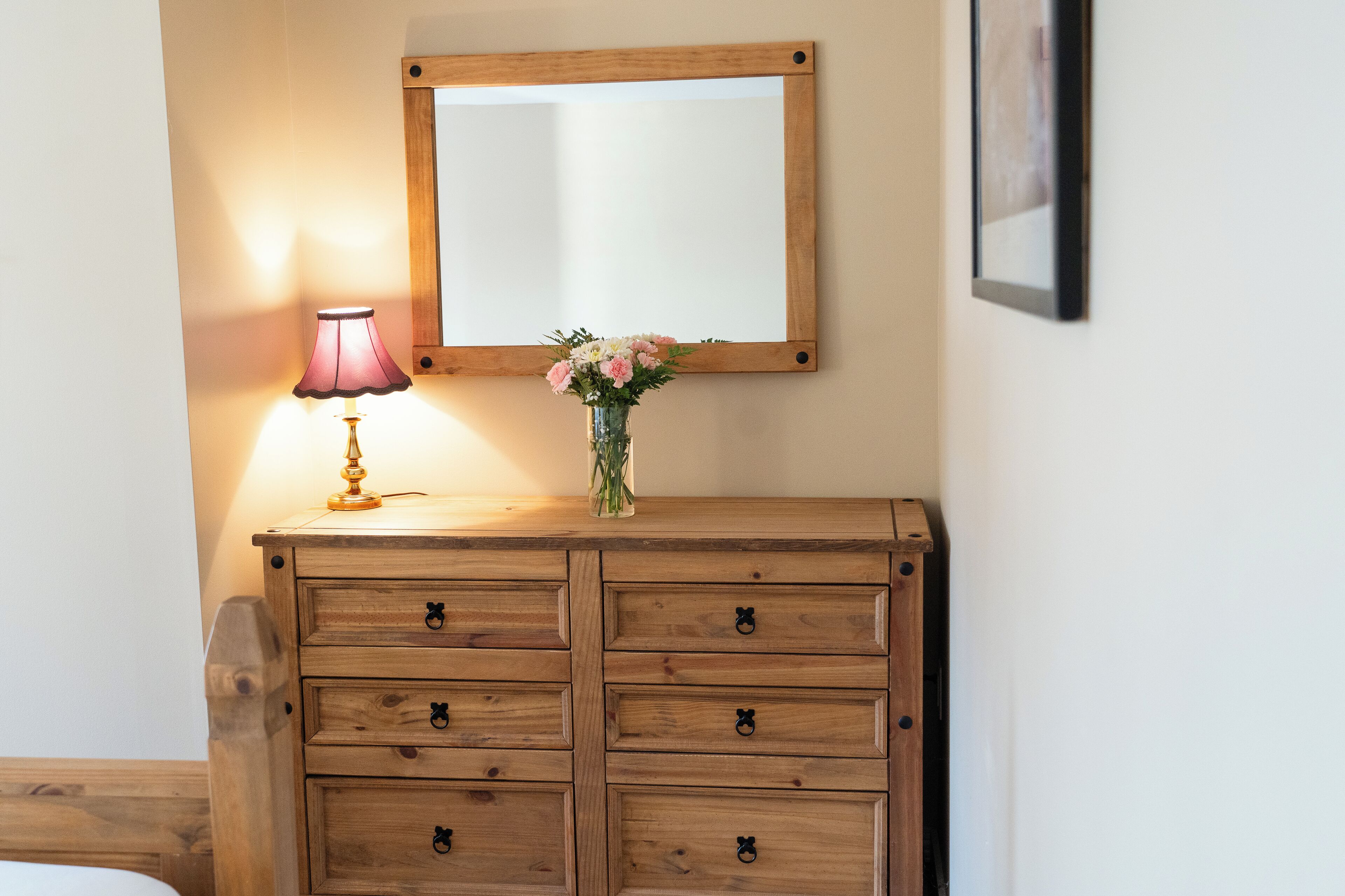 Une commode en bois avec de nombreux tiroirs, un miroir au-dessus et un vase rempli de fleurs sur le dessus.