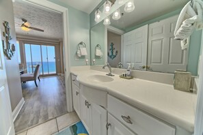 A bathroom with a large mirror, a sink, and a ceiling fan. There is a view of a balcony through the door.