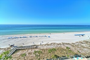 A beach with a wooden boardwalk leading to a sandy area with blue umbrellas and lounge chairs.