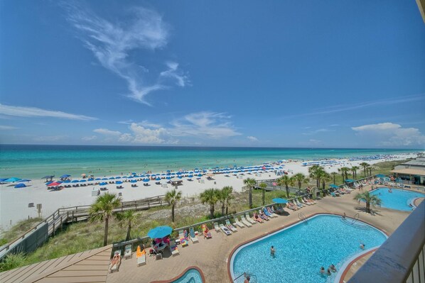 A beach resort with a pool area, beach umbrellas, and a clear view of the ocean.