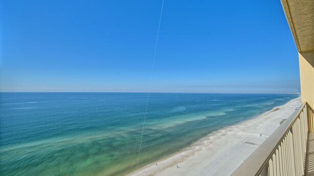 A beach view from a balcony with a clear sky and calm sea.