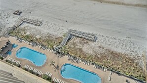 An aerial view of a resort with two swimming pools, a beach area, and a lifeguard tower.