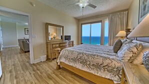 A bedroom with a large bed, a ceiling fan, a dresser, a desk, and a view of the ocean. - Gulf Crest 2006- 20th Floor Living w/ Beach Service (Panama City Beach)