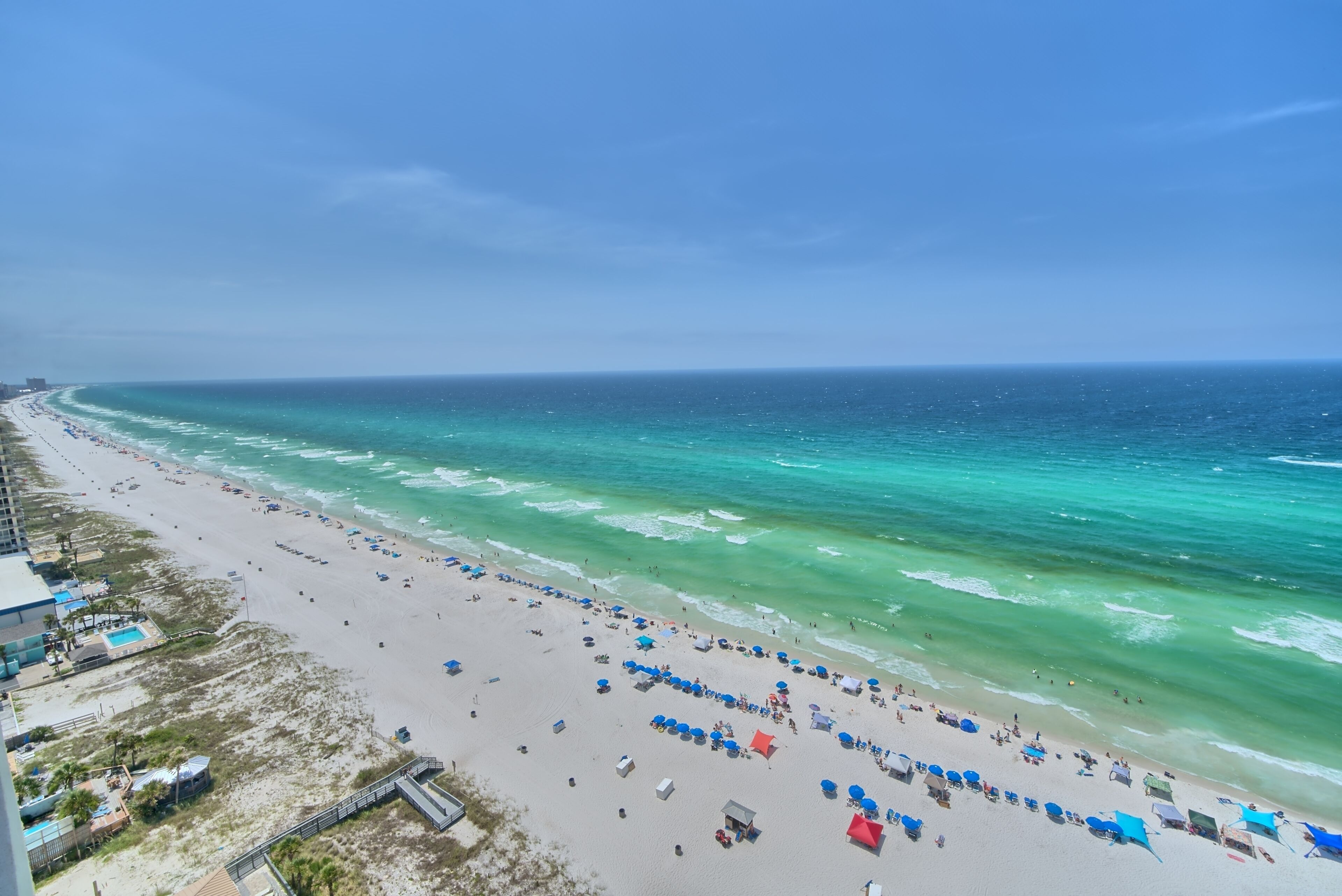 A beach with rows of umbrellas and beach chairs, a sandy shore, and the ocean.