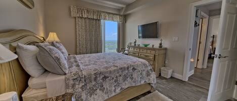 A bedroom with a bed, a TV, a ceiling fan, a nightstand, and a view of the outdoors.