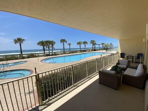 A pool area with multiple swimming pools, a beach view, and outdoor seating.