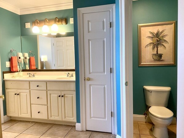A bathroom with a white vanity, a sink, a toilet, and a framed picture of a palm tree on the wall.