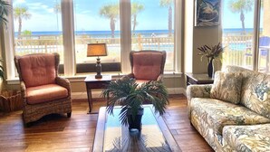 A living room with a view of the ocean, featuring two wicker armchairs, a floral sofa, and a glass coffee table. - Gulf-Front Escape | 1st Floor + 2BR (Panama City Beach)