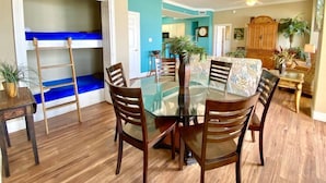 A dining area with a glass table, wooden chairs, a bunk bed, and a ceiling fan. - Gulf-Front Escape | 1st Floor + 2BR (Panama City Beach)