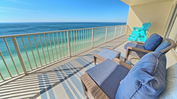 A balcony with wicker furniture, a view of the ocean, and a turquoise chair. - Gulf Crest 2304 | Your Gulf-Front Home Away From Home! (Panama City Beach)