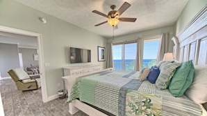 A bedroom with a large bed, a ceiling fan, a television, and a view of the ocean. - Gulf Crest 2304 | Your Gulf-Front Home Away From Home! (Panama City Beach)