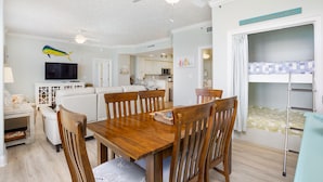 A dining area with a wooden table and chairs, a ceiling fan, and a television in the background.
