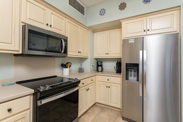 Una cocina con armarios de colores claros, un refrigerador de acero inoxidable, un microondas y una estufa.