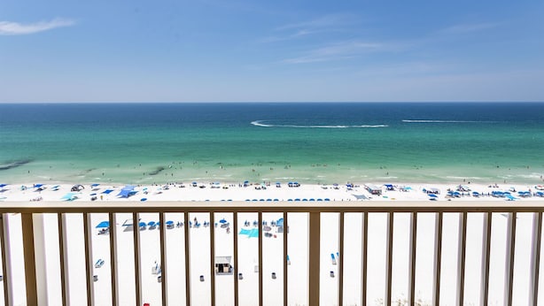 A beach view with a clear sky, calm sea, and a sandy shore with umbrellas and beach chairs.